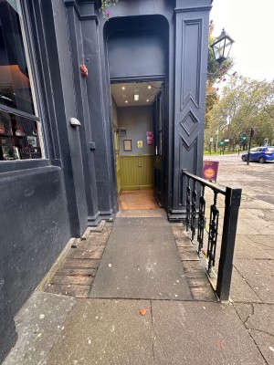 Ramp to entrance. Single manual wooden door. Push from left.
