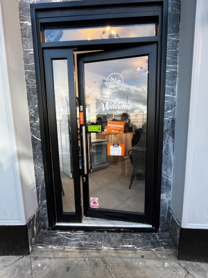 Glass door with black frame. Push from left to open. One step up to door followed by another step up at foot of door.