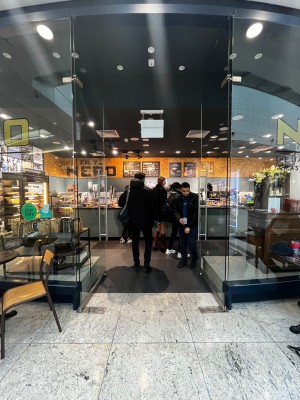Facing glass doors ahead. Push handles in center to open.