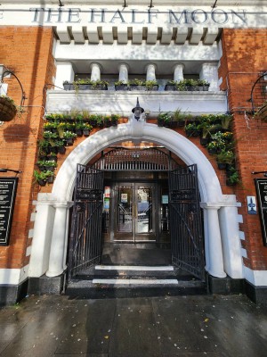 From street, facing venue. Black, metal gates ahead kept open. Steps up at gate.