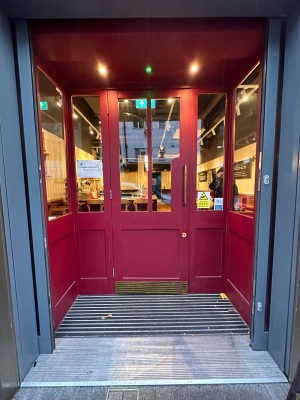 Sliding glass doors with grey frame propped open ahead. Red wooden door with glass panels at back. Pull golden, metal handle on right to open.