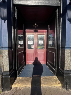Glass double doors with black frame. Push from middle to open. Doormat after first set of doors.