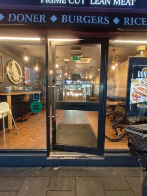 Facing black framed glass door. Push silver metal handle on left to open.