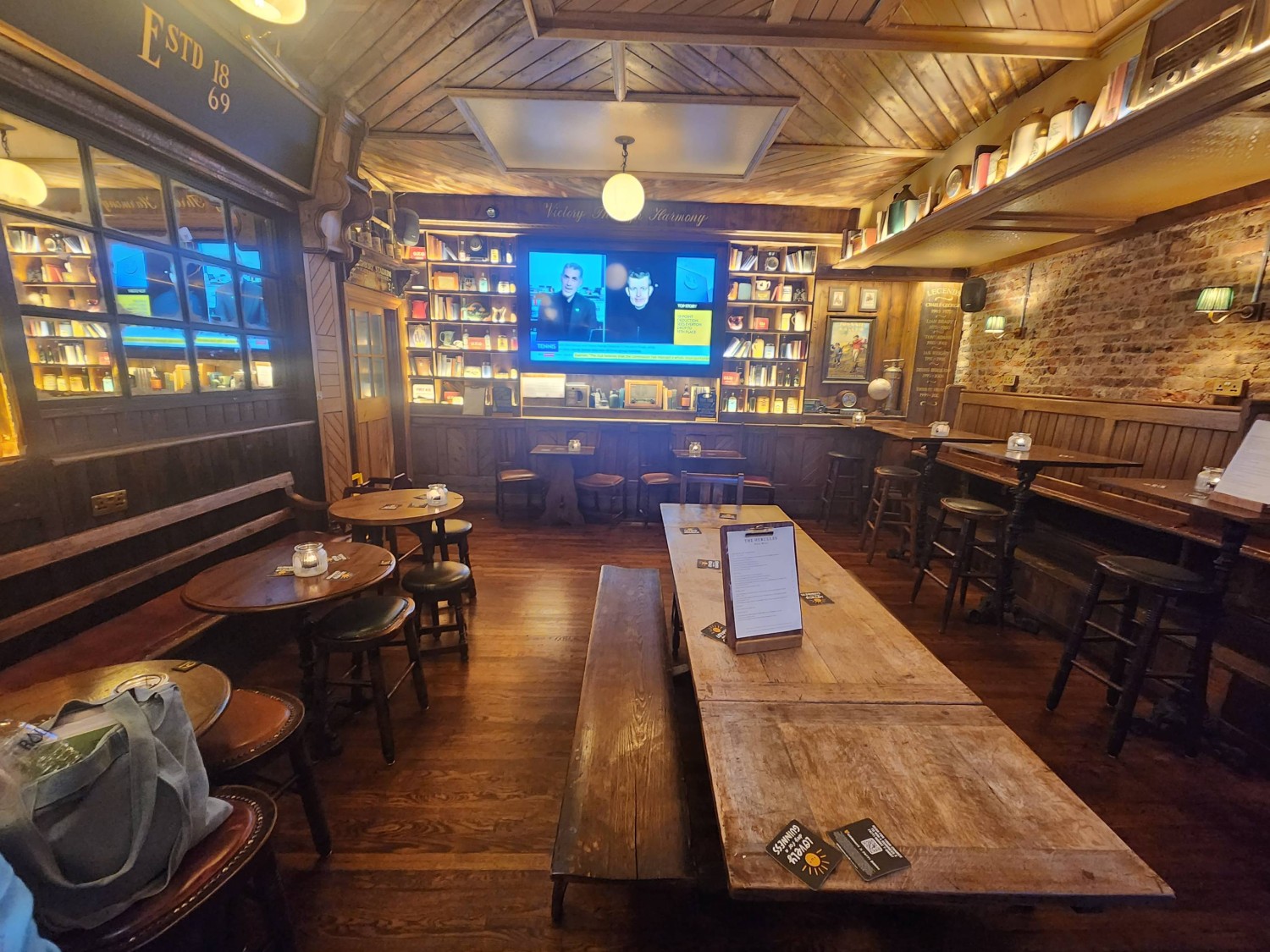From beginning of new path, looking straight. Bench with table and chair on right. Half booths with high tables and stools along far right wall.