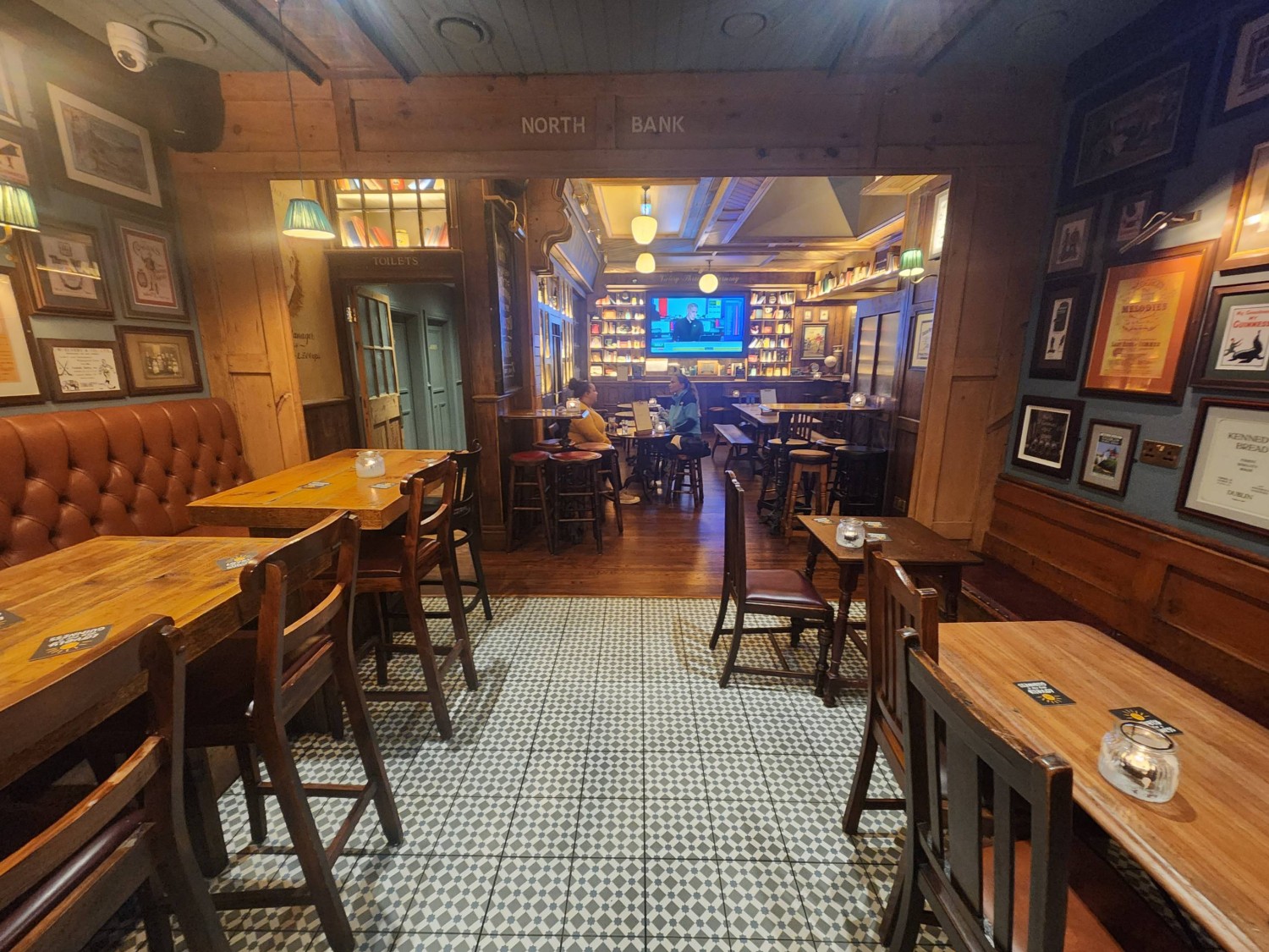 From middle of path, looking straight. Half booths with high tables and chairs on left of path. Half booths with tables and chairs on right of path.