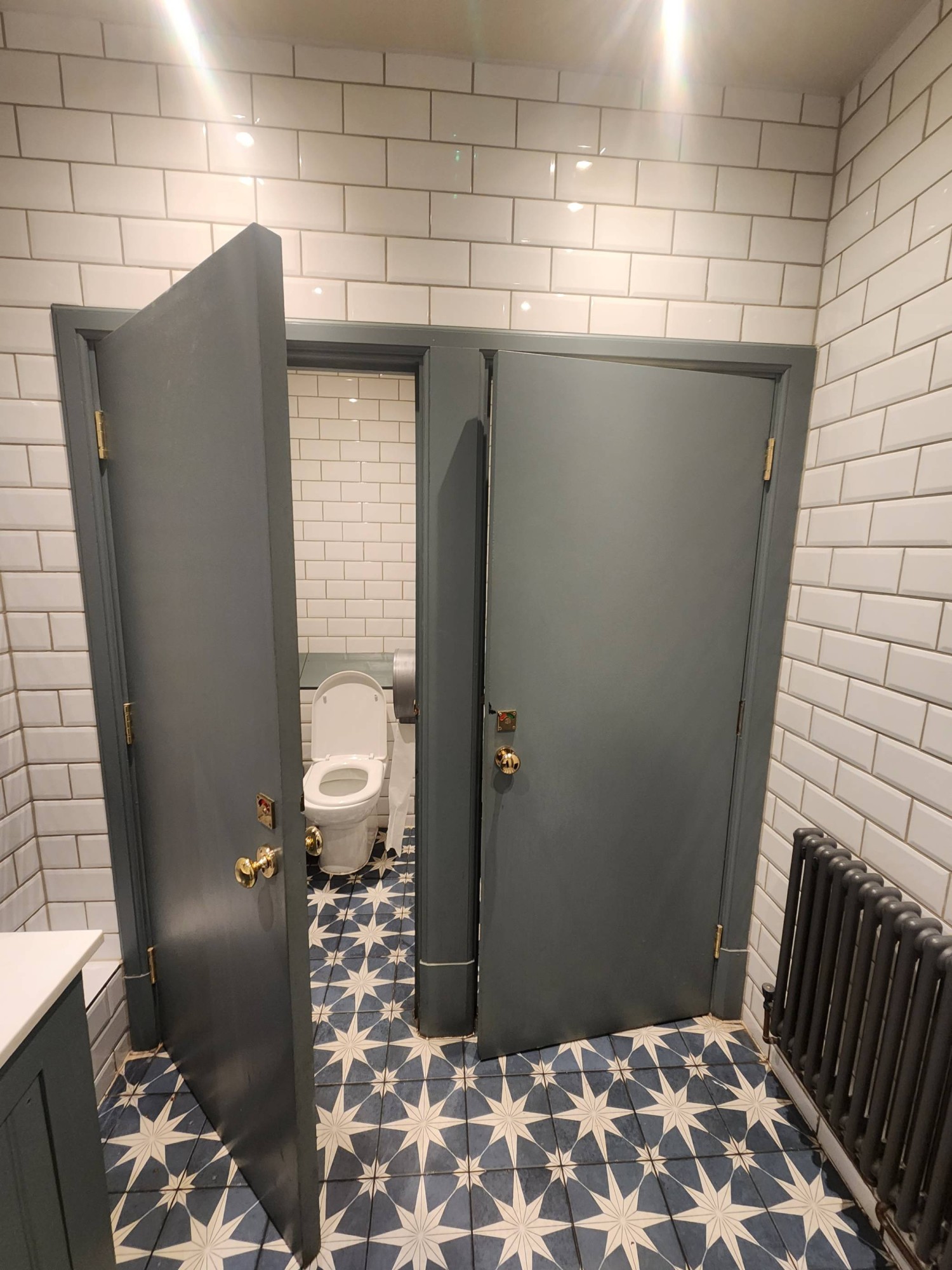 From door, looking right. Two cubicle doors ahead. Handle on left for right cubicle. Handle on right for left cubicle. Pull to open.