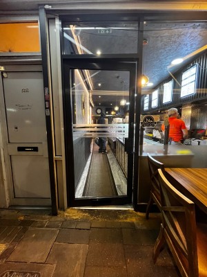Glass door with black frame. Push from right to open. Small built in ramp leading to door.