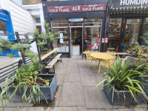 From street, looking straight at cafe. Path leading forward to entrance ahead. Plant pots on either side of path beginning.