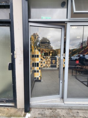 Glass door with metal frame. Handle on right. Push to open.