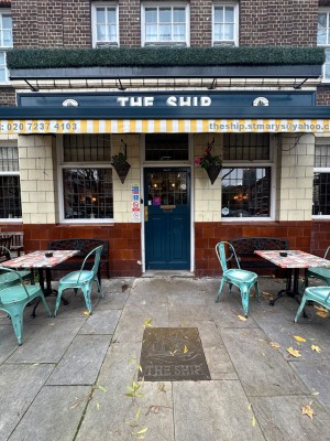 From pavement facing venue. Tables with chairs on left and right. Path to entrance at centre.