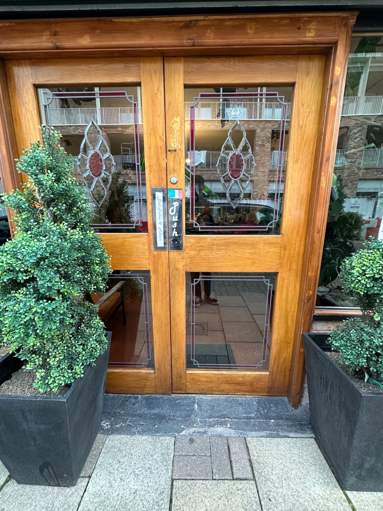 Double glass door. Manually operated, push centre to open. 
Decorative plants either side of the door.