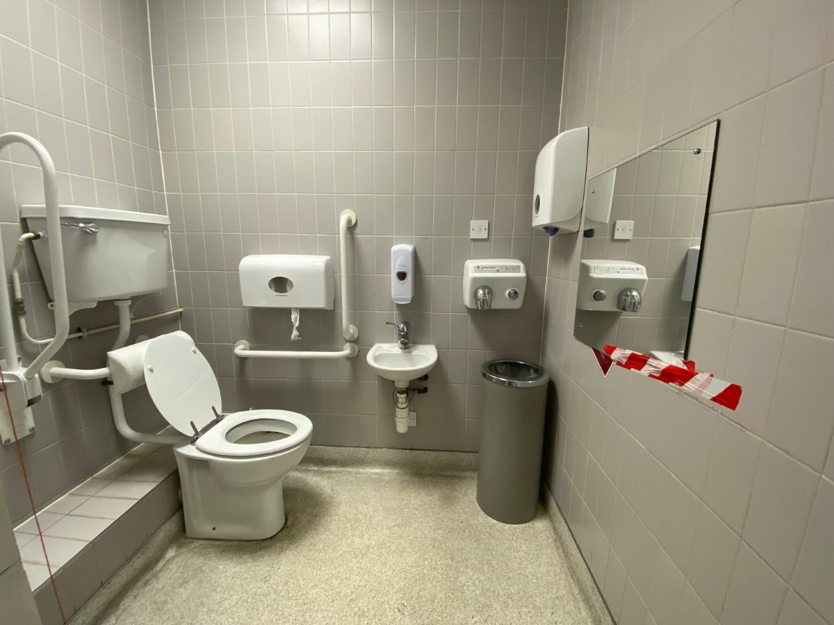 From doorway, facing straight. Sink at back. Toilet on left. Emergency pull cord to it's left.