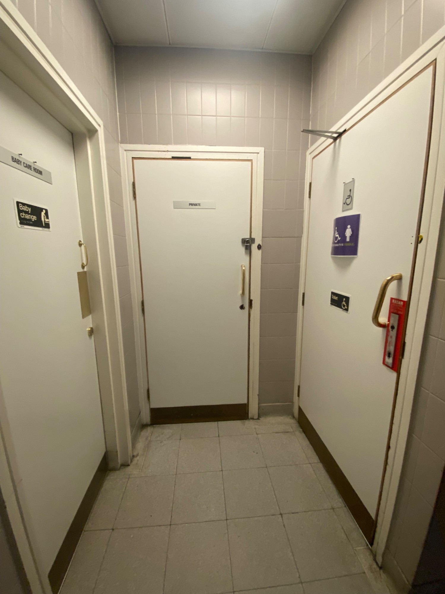From opening, looking right. Baby change room on left. Pull golden handle on right to open. Accessible bathroom on right.