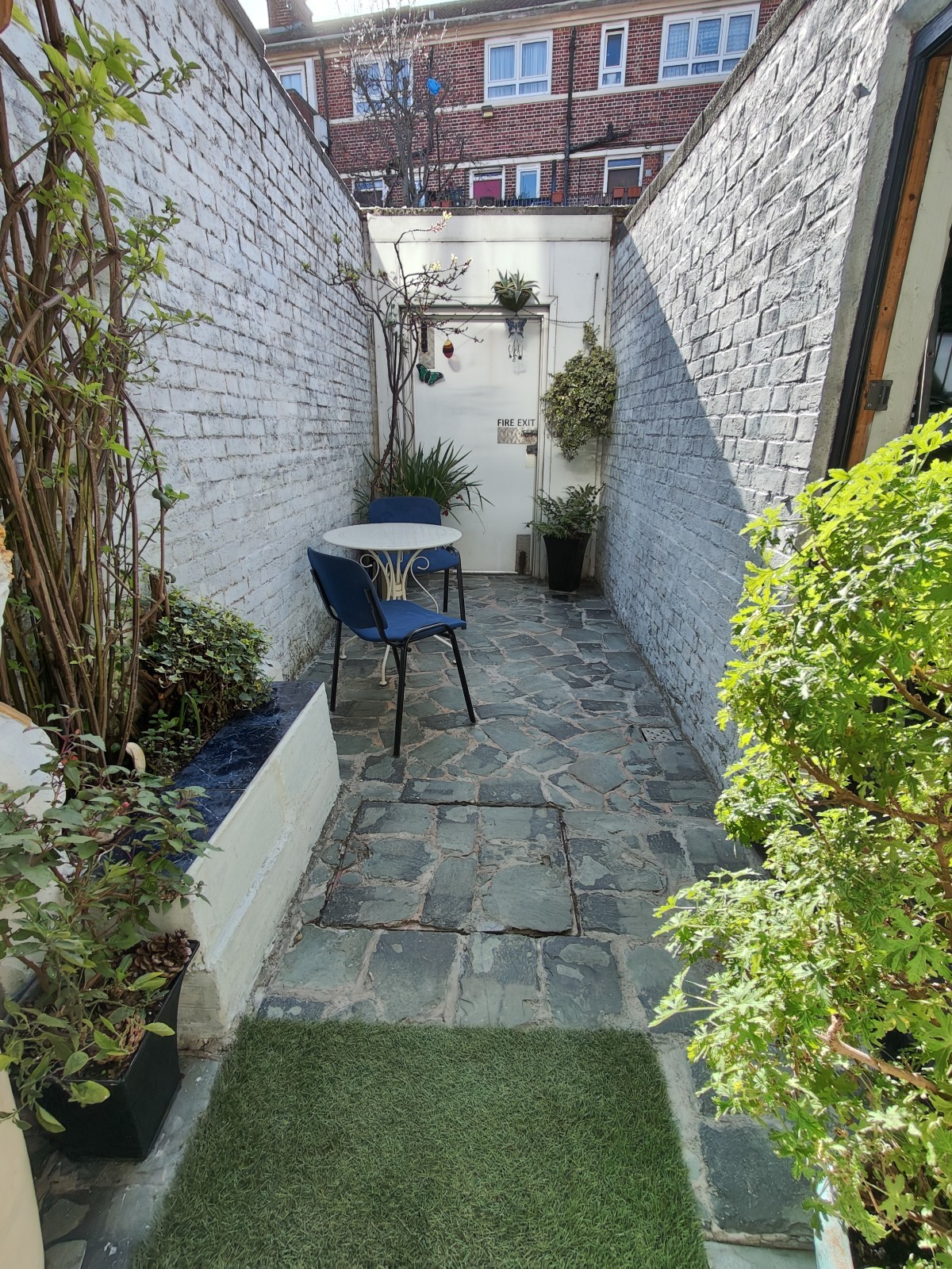 From door facing straight. Planters on left and right. Path ahead to table and chairs on left.