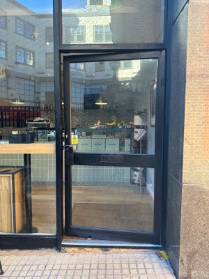 Glass door with black frame, push from left to open.