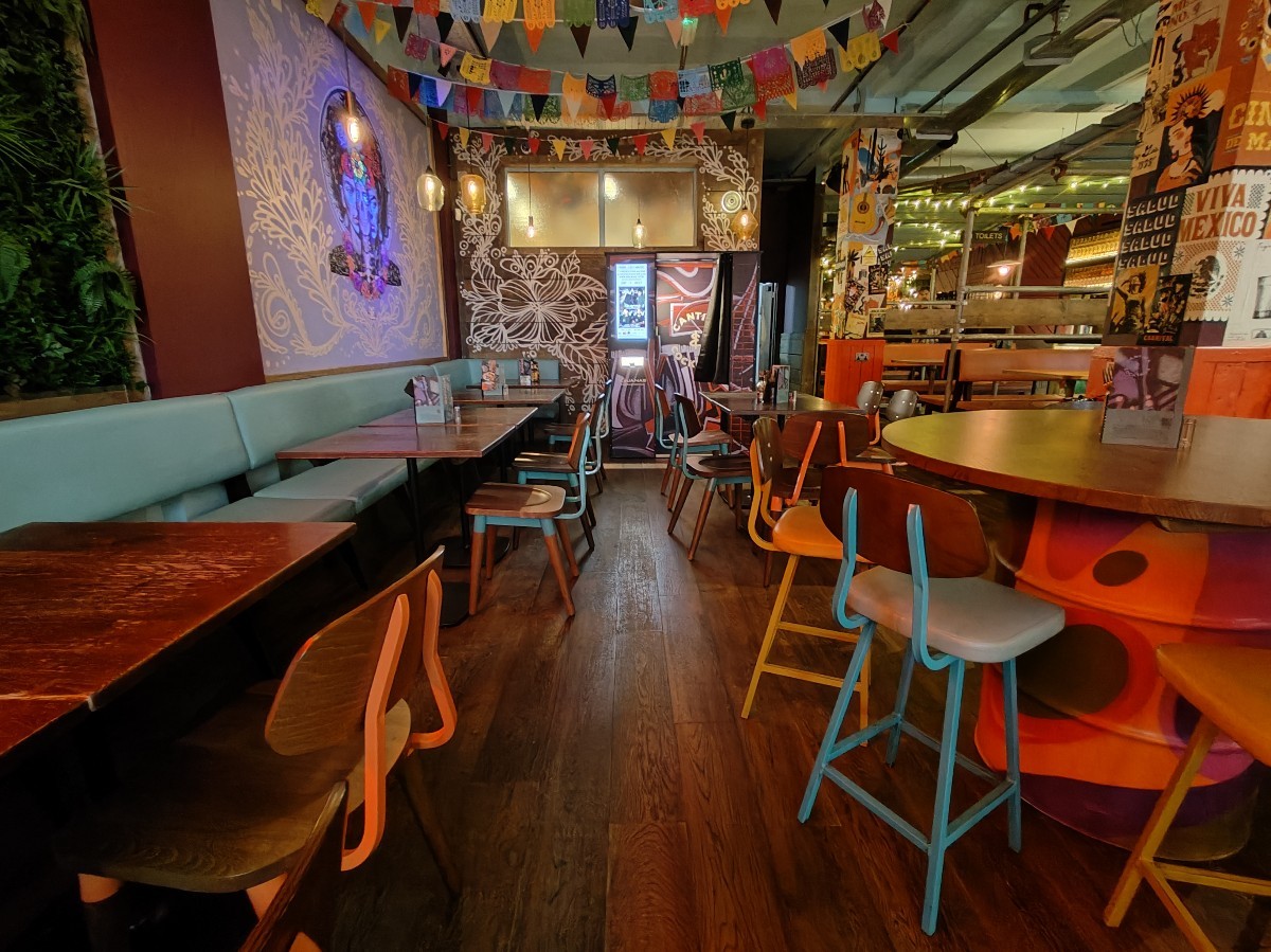 From before half booths facing right. High table and stools on right. Table and chairs beyond. Half booth along left.