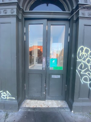 Small bump before doorway. Then grey and glass double doors straight ahead. Push from middle to open.