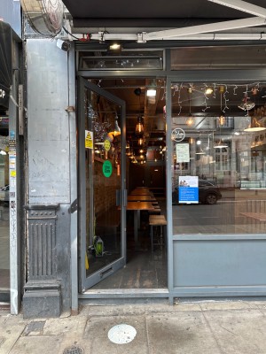 Facing glass door with gray frame. Push handle on right to open.