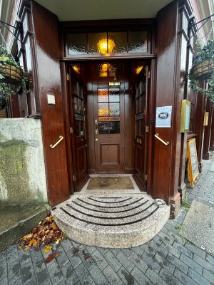 One step up to glass double doors with brown wooden frame. Push from middle to open. Glass door with wooden frame immediately after. Pull from left.