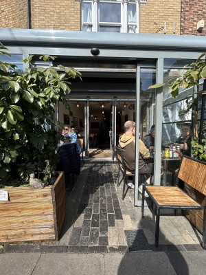 Preceding sliding glass doors with grey frame. Push from middle to left and right to open. Chair on right. Tables and chairs inside on both sides.