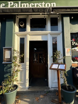 From sidewalk facing venue. White framed archway ahead. Venue menu baord on right.