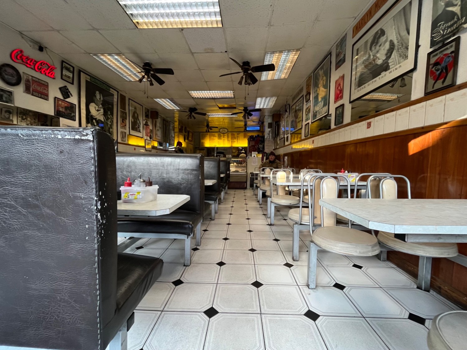 From right of entrance facing straight. Booths to left. Path in centre to counter at back. Fixed chairs and tables to right.