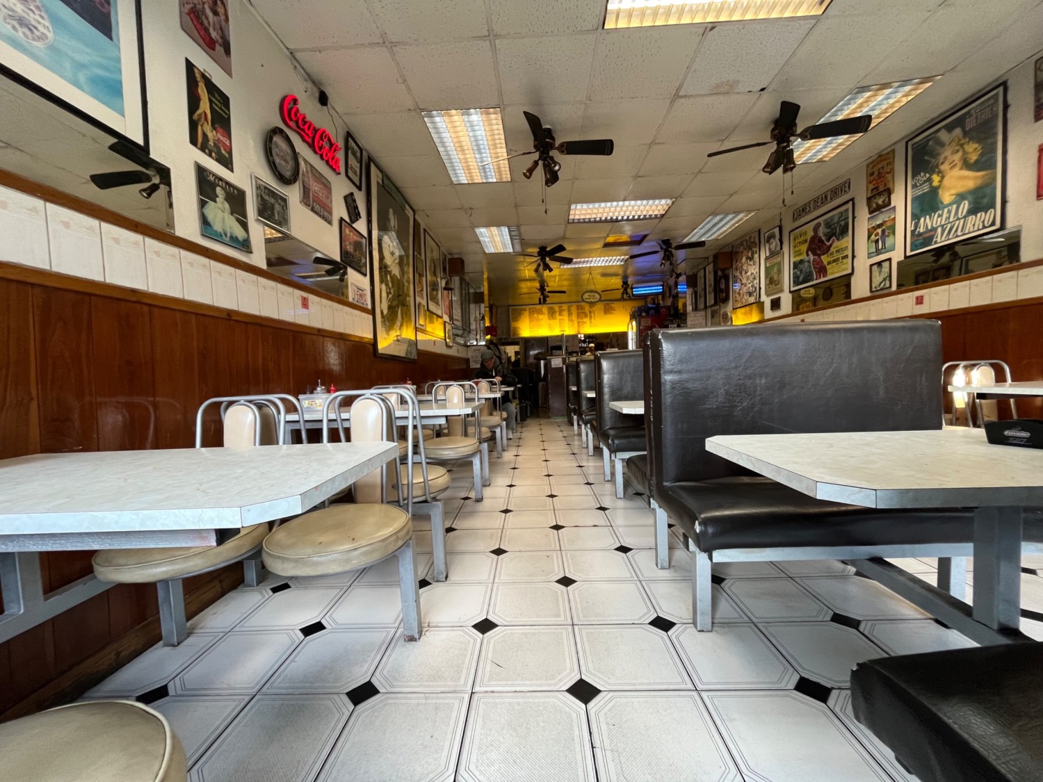 From left of entrance facing straight. Fixed tables and chairs to left. Path in centre to counter at back. Booths to right.
