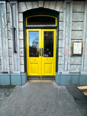 Facing glass paneled doors with bright yellow frame. Pull sliver handles in center to open. Built in ramp up ahead of entrance.
