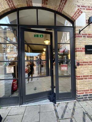 Glass door with black metal frame. Push handle on right to open.