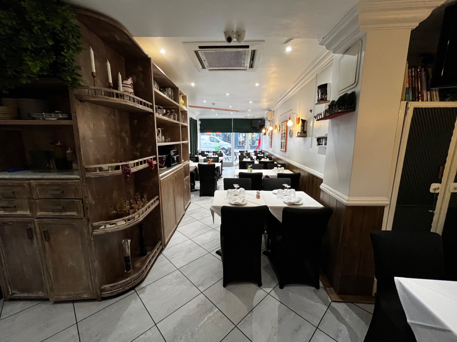 Facing left at tables on wall. Tables with chairs along right wall ahead. Path to left continues to more seating.