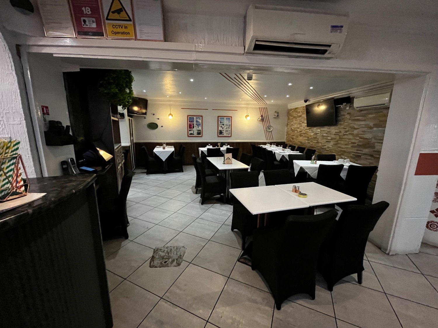 Facing left before path to bathroom. Tables with chairs to right, on right wall, and on wall ahead. Path ahead continues left at tables on wall.