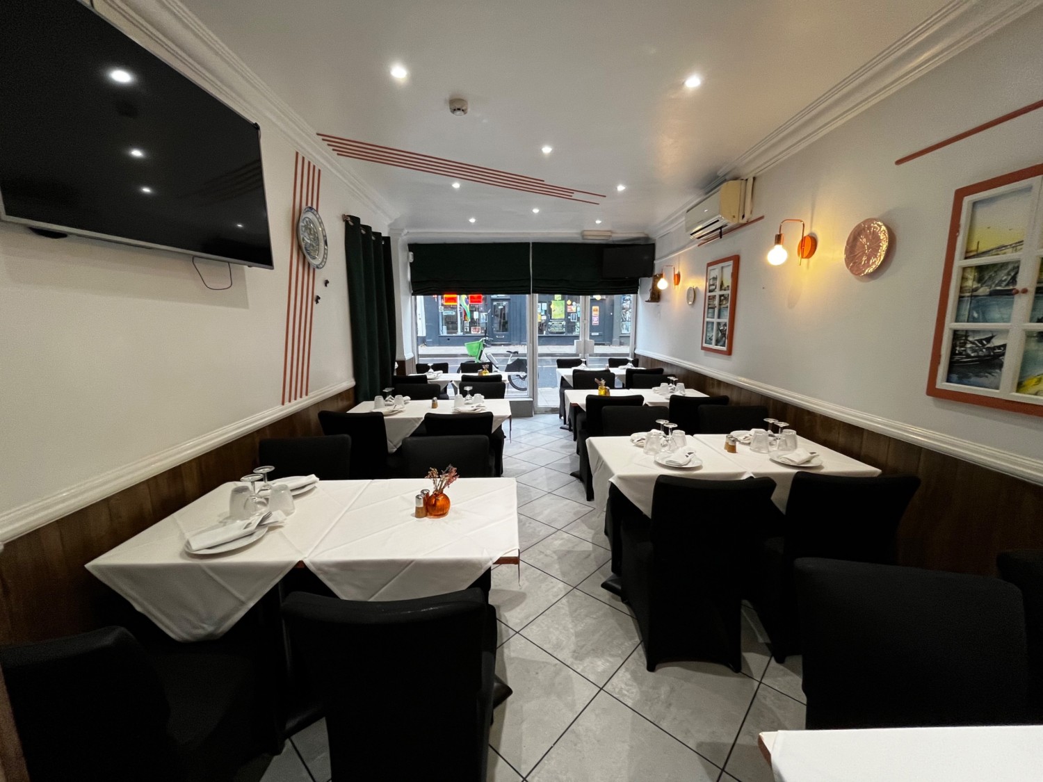 From narrow path facing straight on. Tables with chairs on left and right walls, path between them.
