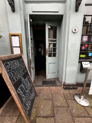 Glass double doors with pale blue frame. Pull from middle to open. Advertising board slightly obstructing on left.
