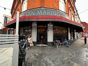 From street, main entrance straight ahead. Fenced outdoor seating to left and open outdoor area to right.