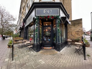 From street corner, entrance door straight ahead. Outdoor seating areas either side of entrance.