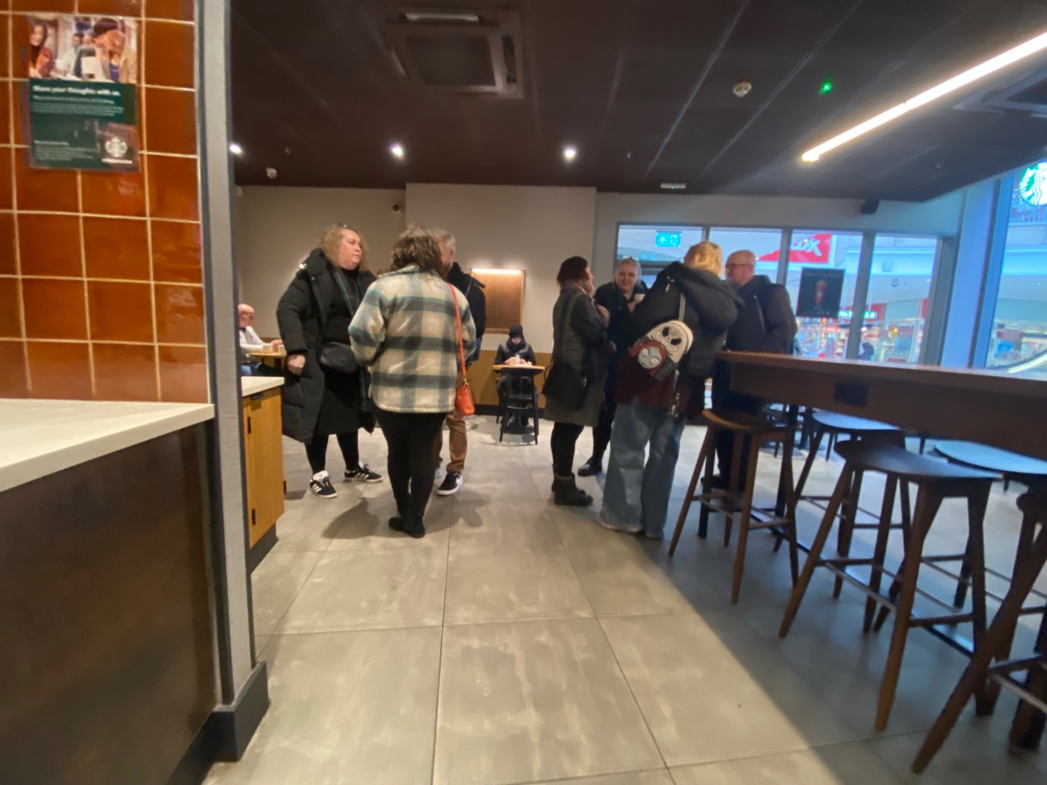 Further up path. Path continues straight. Counter along left. High tables, stools along right. Side entrance in centre of back wall.