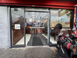 From street, facing main entrance. Double glass doors with grab handles towards centre. Push to open.