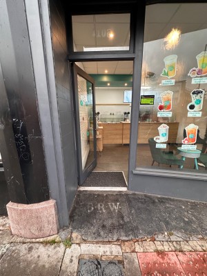 Glass door with grey wooden frame ahead. Push metal handle on right to open.