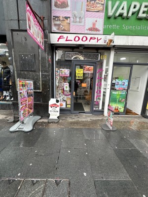 From street, facing shop front. Glass door with handle on left. Pull to open.
