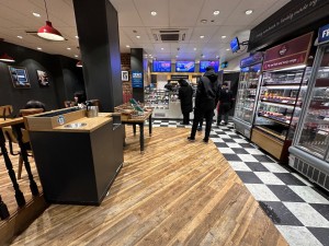 From entrance, looking straight ahead. Fridges on left. Open waiting area and counter on right. Seating on left after barrier.
