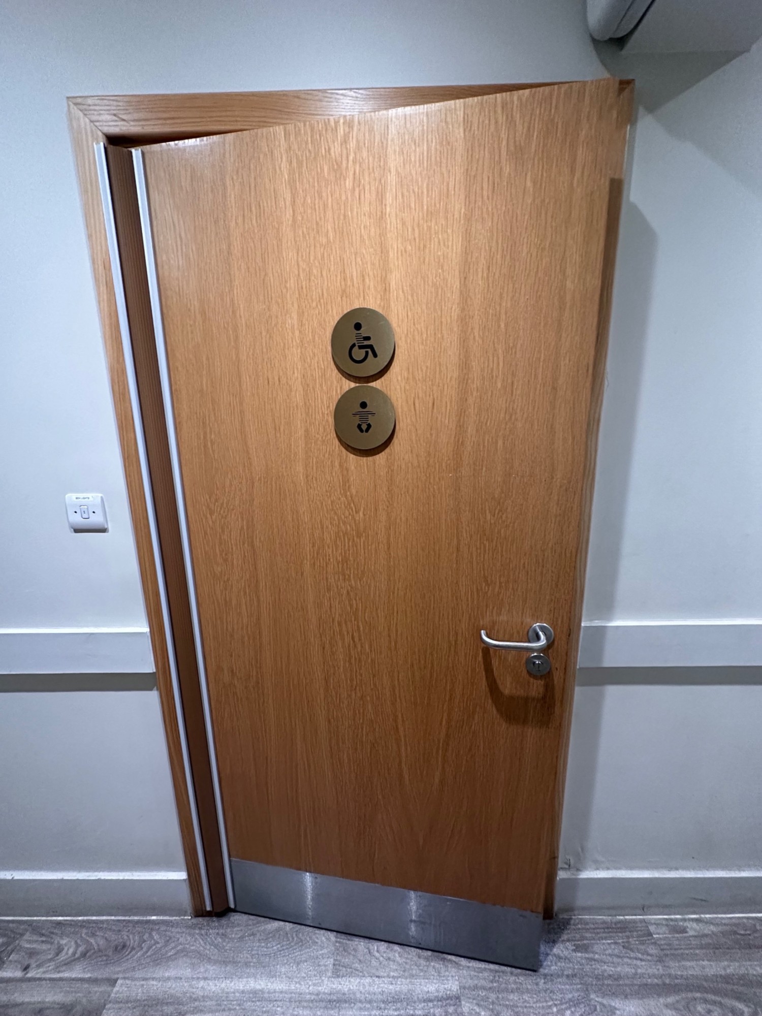 From first door facing straight. Wood door ahead with white frame and metal handle. Pull from right to open.