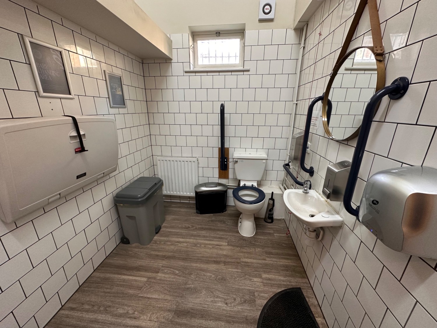 From second door, facing straight. Baby change on left. Toilet at back right. Emergency pull cord to its right. Sink on right.