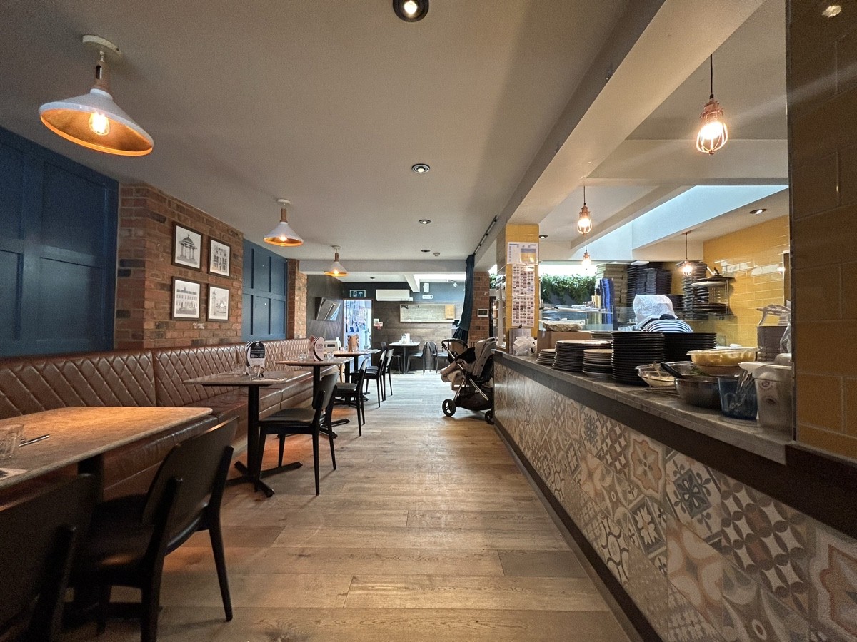 From end of booth facing straight. Half booths along left. Open kitchen along right. Path in centre to back area.