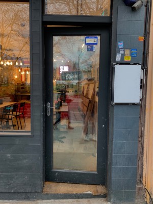 Glass door with black wooden frame. Push handle on left side to open.