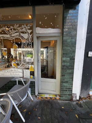 Glass door with white wooden frame. Push from left to open. Small step up then down through door.