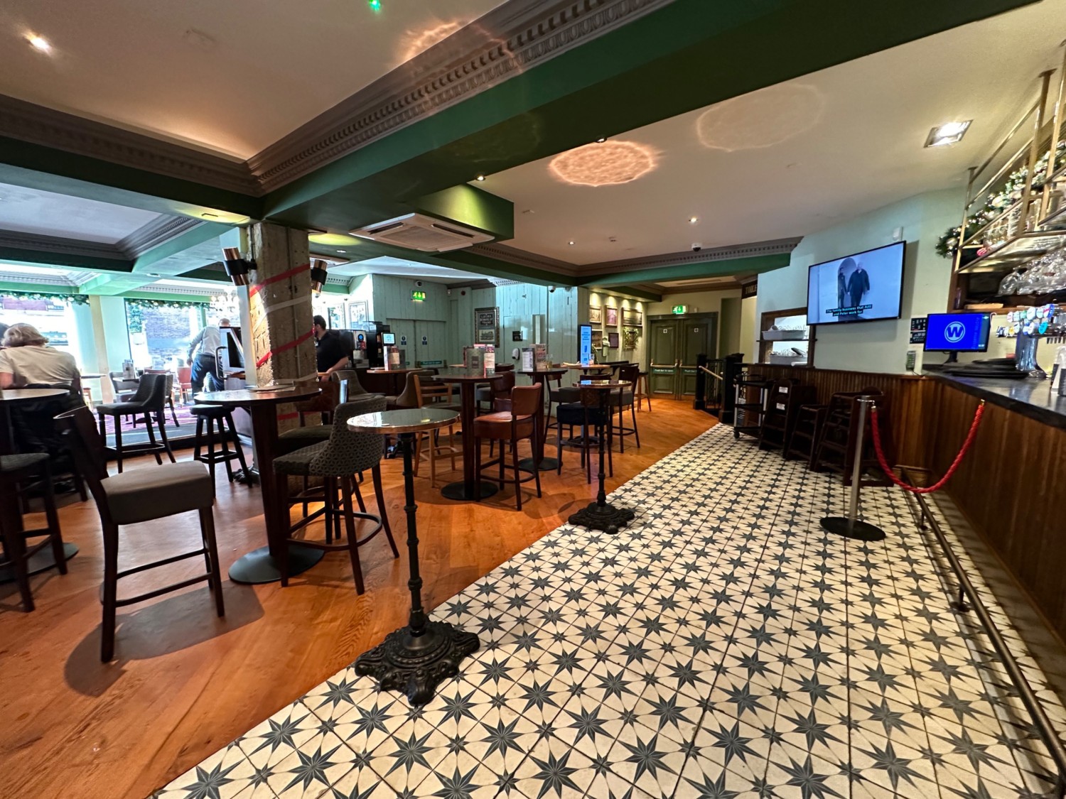 From end of bar facing straight. Path down center to bathroom on back left. High tables, chairs and stools along left. Column to their left.
