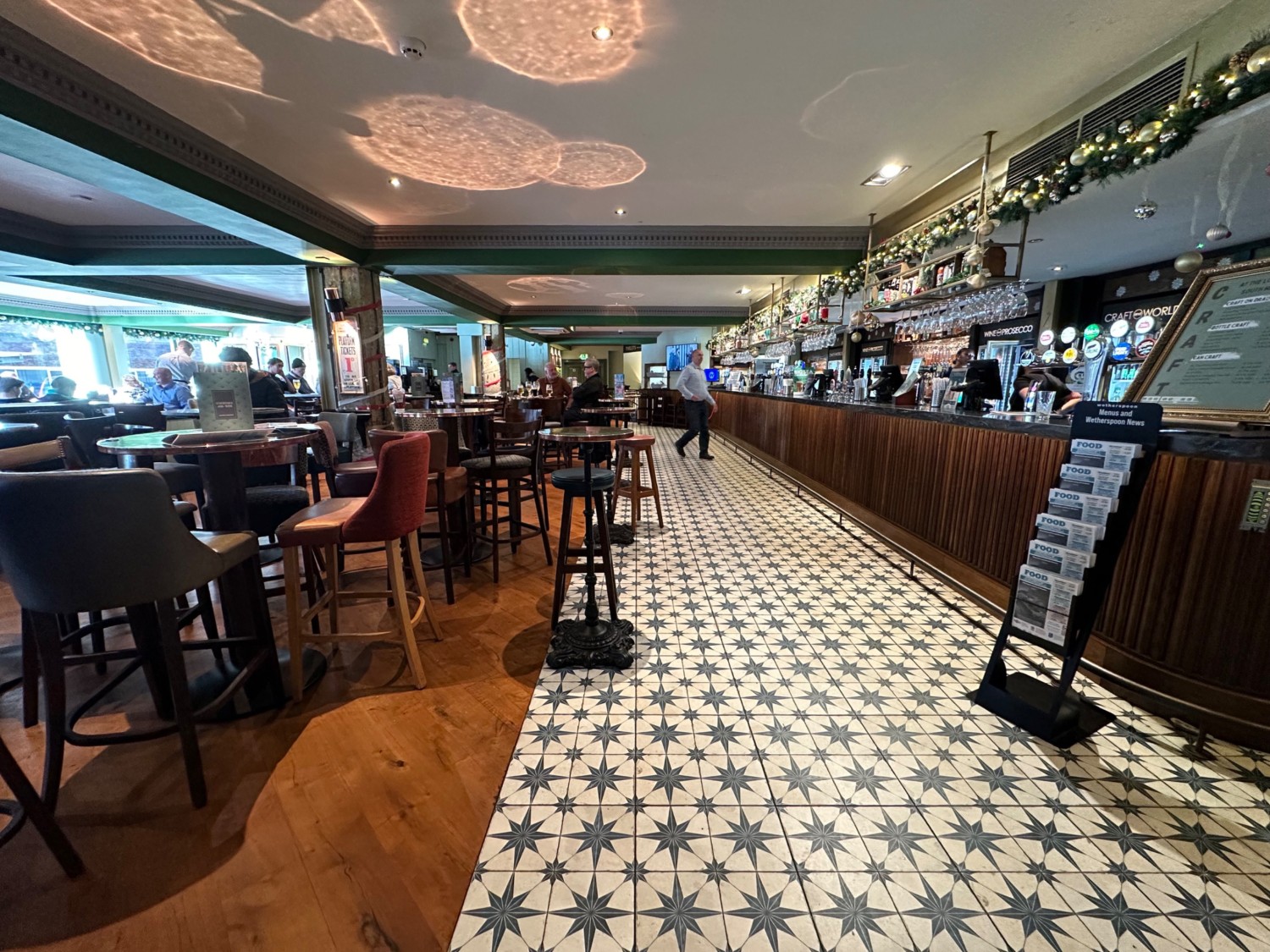 From bar facing left. Bar along right. High tables, chairs and stools along left.