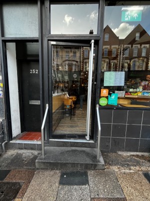 Glass door with black frame. Push from right to open. Two steps up to door. Handrails on left and right.