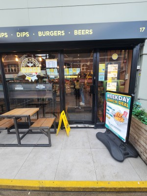 From street, facing venue. One step up to platform. Glass door at the back. A-frame sign on right.