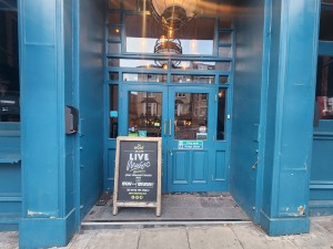 Glass double doors with blue frame. Pull from middle to open. Advertising board obstructing left door.